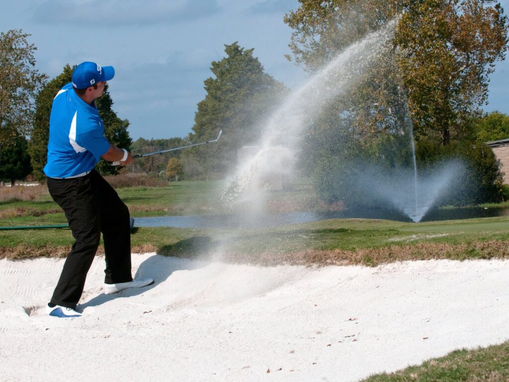 Golfer hitting out of a sand bunker on a tree-lined course